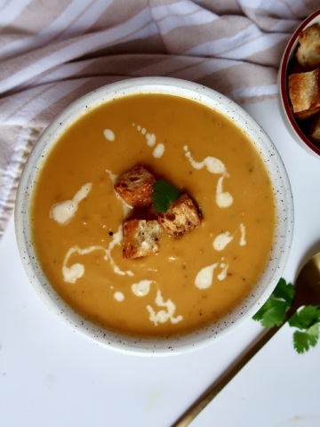 Blended sweet potto soup in a white bowl with croutons on top and coconut milk drizzled inside.