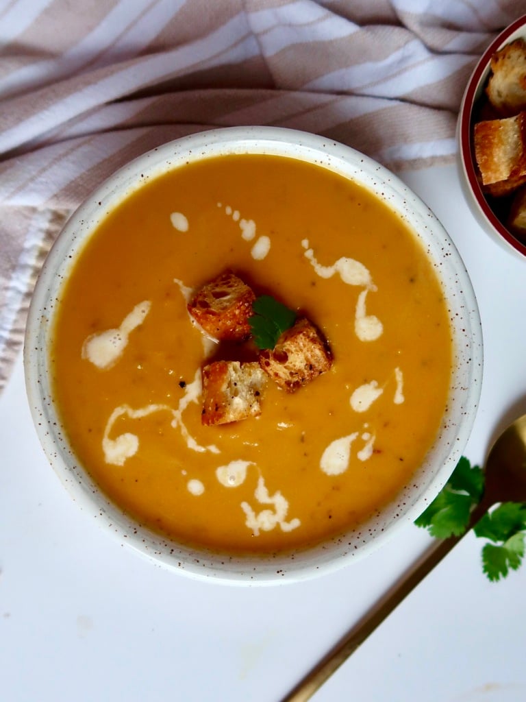 Blended sweet potto soup in a white bowl with croutons on top and coconut milk drizzled inside.