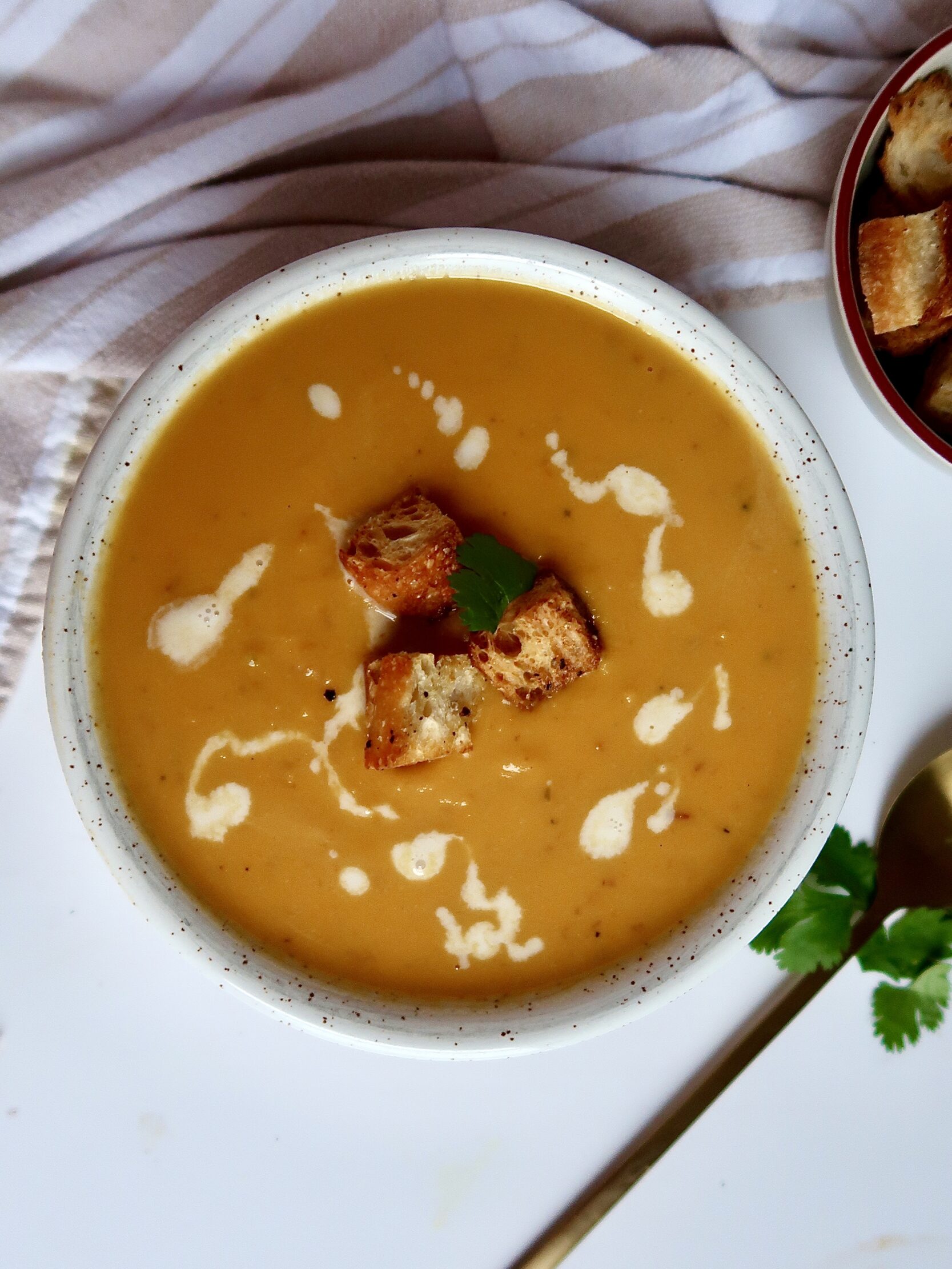 Blended sweet potto soup in a white bowl with croutons on top and coconut milk drizzled inside.