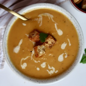Blended sweet potato soup in a white bowl with croutons on top and coconut milk drizzled inside.