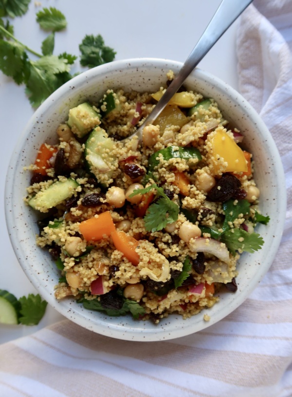 White bowl with couscous, cucumber, bell pepper and chickpeas all mixed together.
