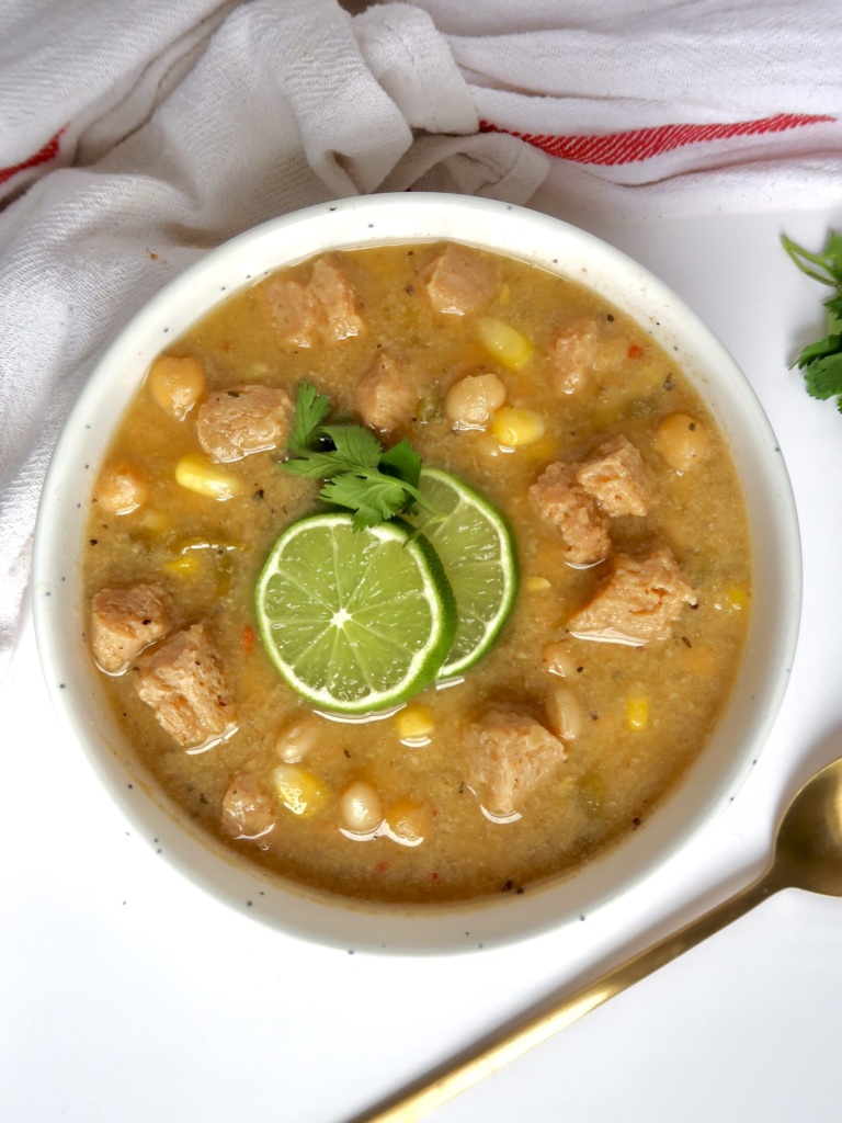 White bowl with creamy base and soy chunks with pieces of corn and beans with lime slices and cilantro on top.