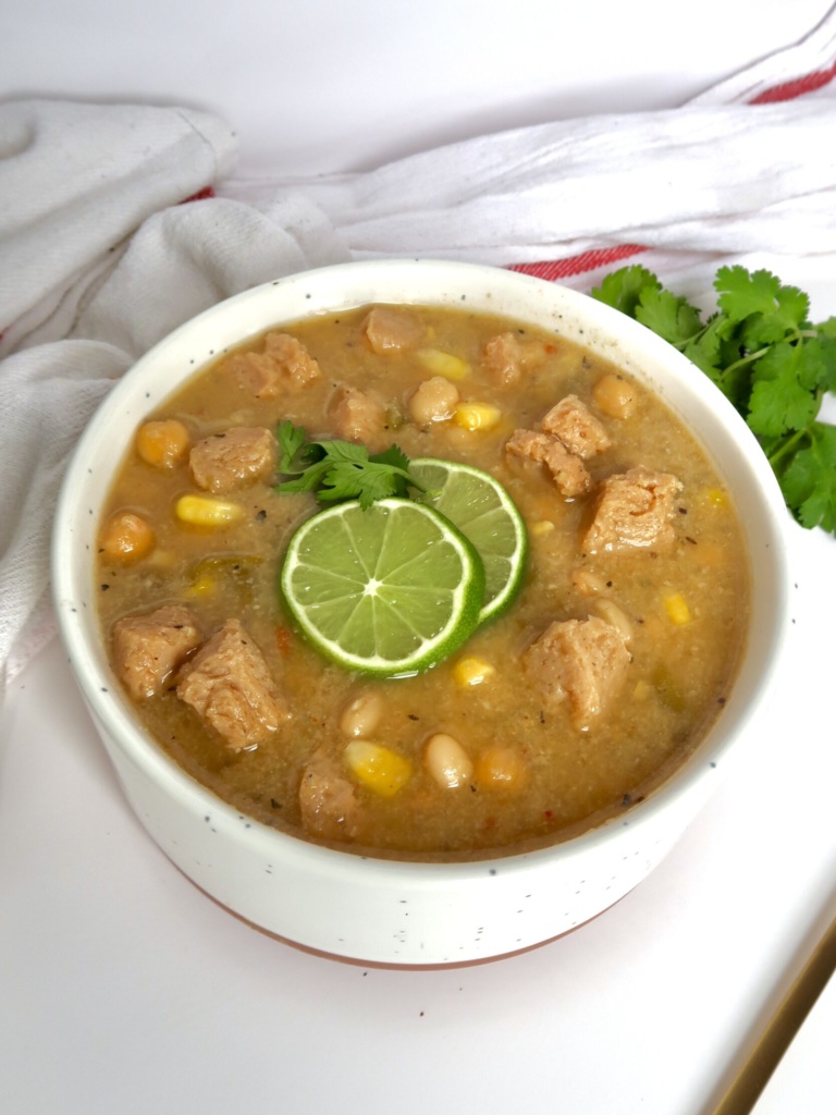 White bowl with creamy base and soy chunks with pieces of corn and beans with lime slices and cilantro on top.