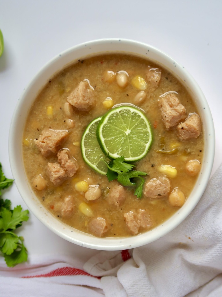 White bowl with creamy base and soy chunks with pieces of corn and beans with lime slices and cilantro on top.