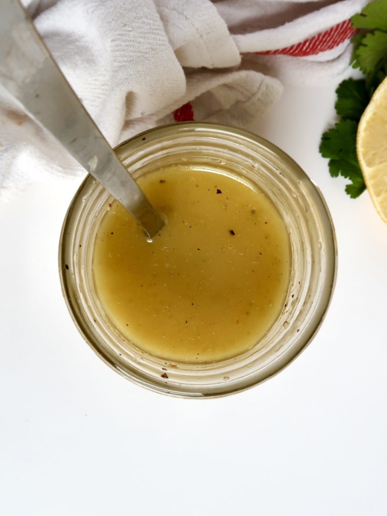 Jar with lemon vinaigrette inside with a spoon in it and lemon to the side.
