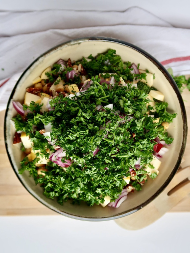 Bowl of sliced apple, pecans, red onion and parsley.