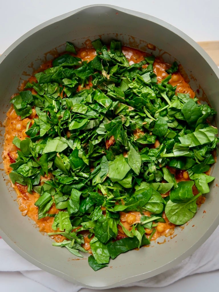 Pan with coconut milk mixed with tomato paste and spinach on top.