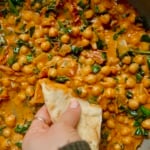 Braised chickpeas in a coconut tomato paste mixture with sundried tomatoes and wilted spinach with a hand dipping naan in it.