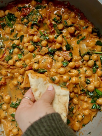 Braised chickpeas in a coconut tomato paste mixture with sundried tomatoes and wilted spinach with a hand dipping naan in it.