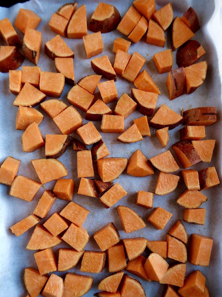 Sheet pan with parchment paper and diced sweet potato on top.