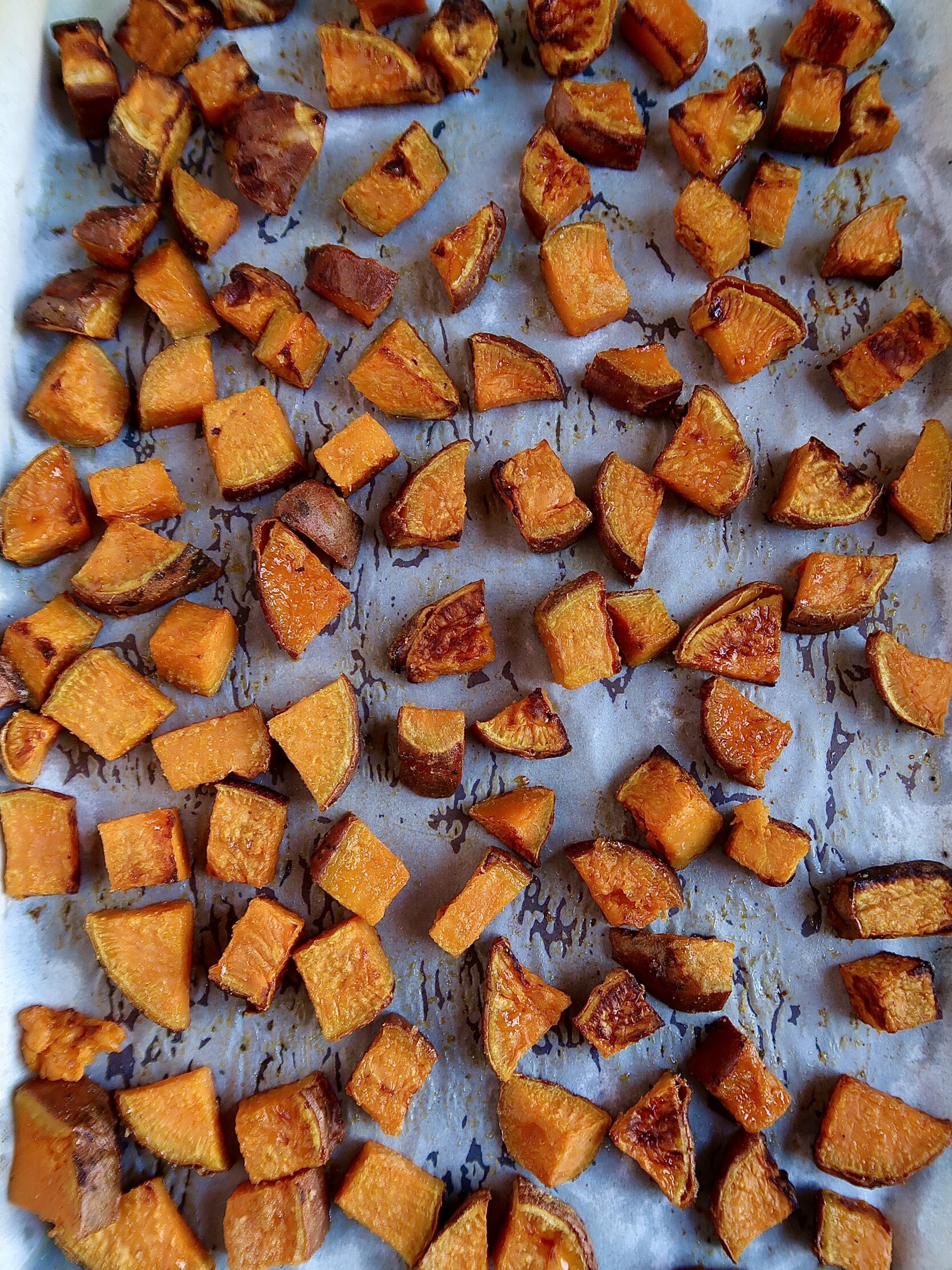 Sheet pan with parchment paper with roasted diced sweet potato on top.