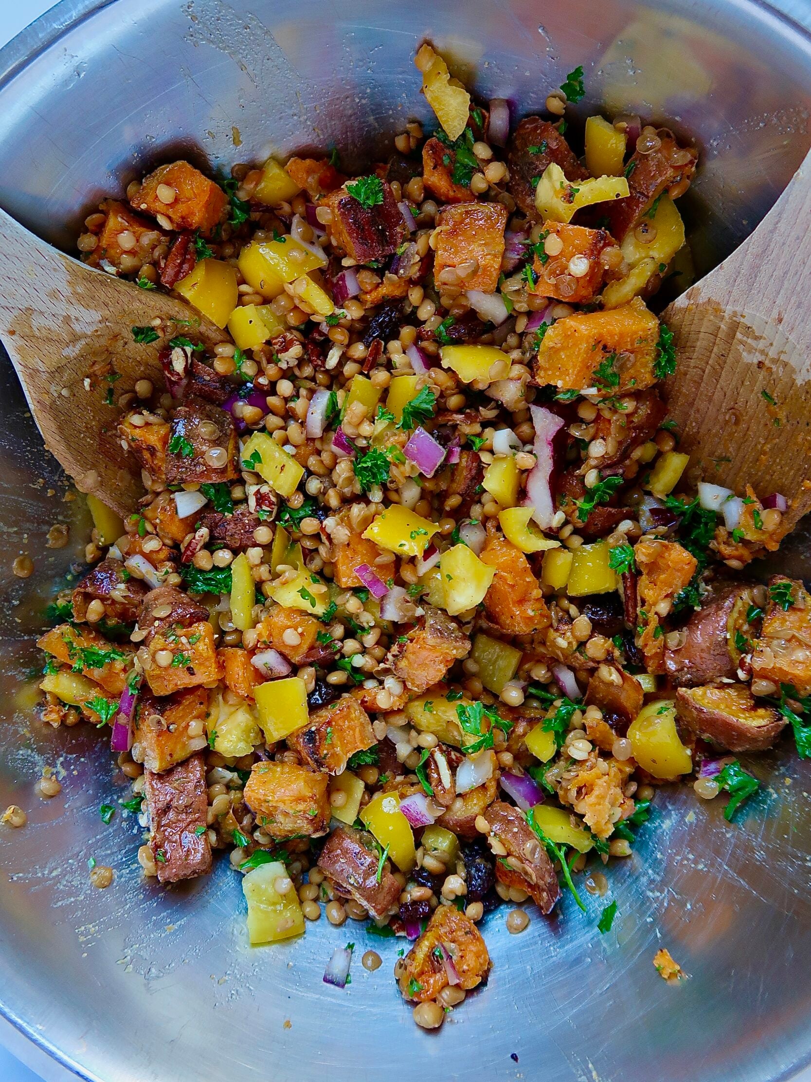 Large bowl with diced sweet potato, lentils, bell pepper, red onion, and pecans inside with wooden spoons.