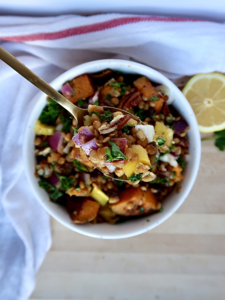 White bowl with diced sweet potato, lentils, red onion, parsley, and pecans and a spoon scooping some.