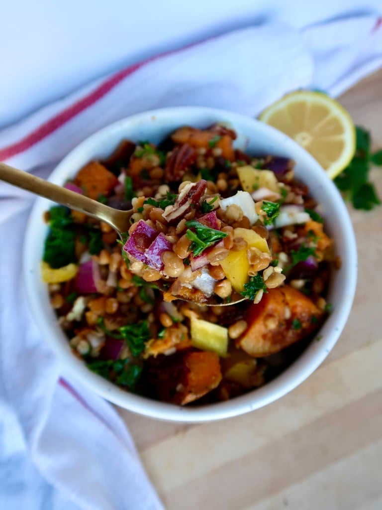 White bowl with diced sweet potato, lentils, red onion, parsley, and pecans and a spoon scooping some.