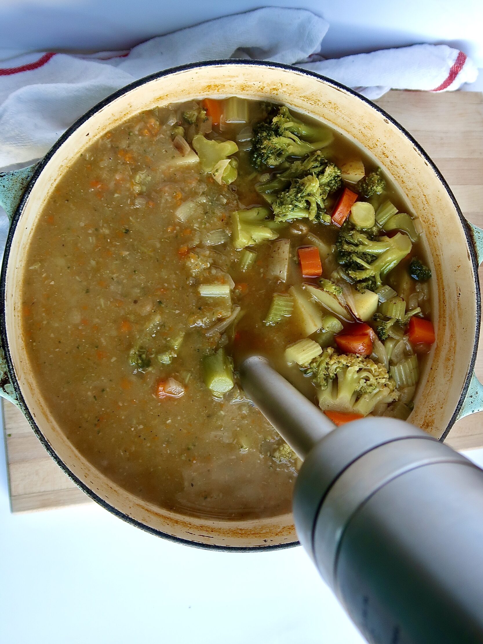 Large pot with carrots, celery, potatoes, broccoli and veggie stock in it with an immersion blender inside and blended half of it.