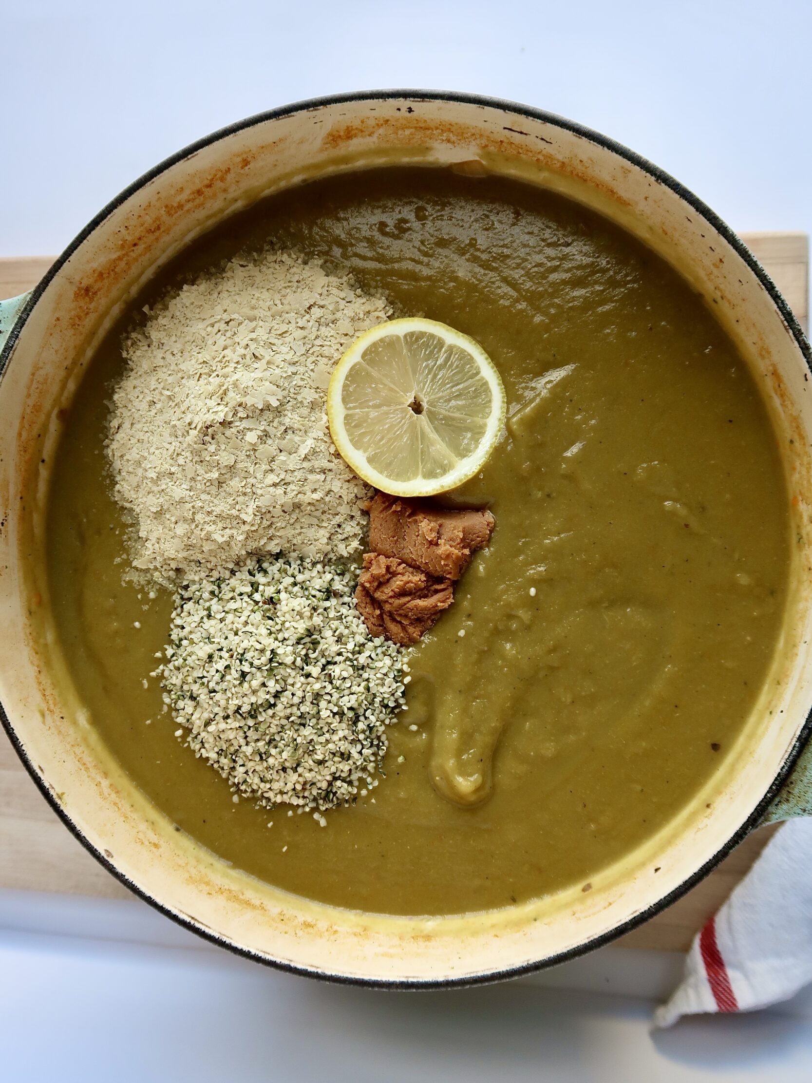 Large pot with blended broccoli soup with nutritional yeast, hemp seeds, miso paste and lemon sliced.