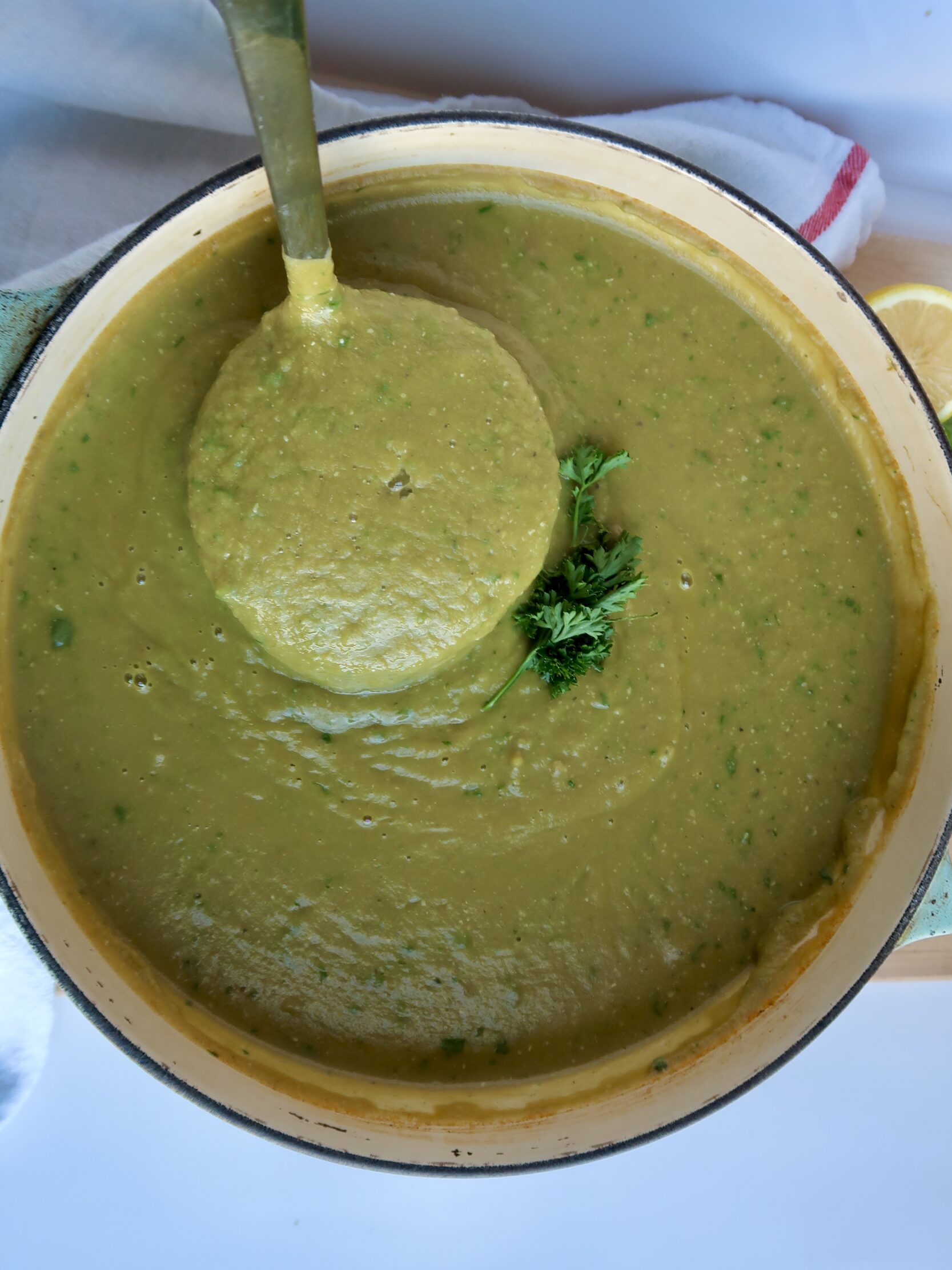 Large pot with blended broccoli soup and parsley to garnish with a ladle scooping some.