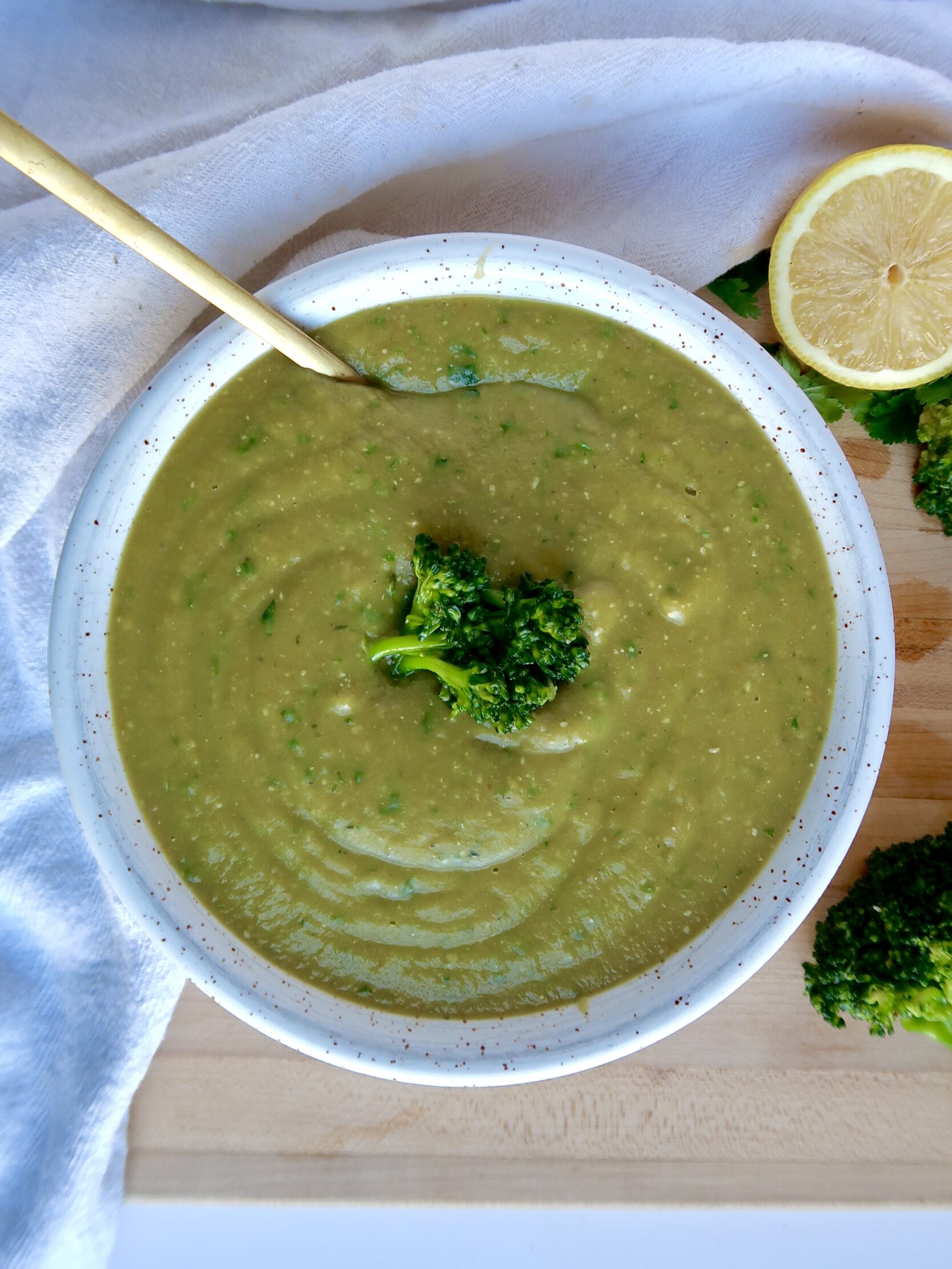 Bowl with blended broccoli soup and parsley too garnish and a spoon inside. 