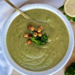 Bowl with blended broccoli soup and parsley too garnish and a spoon inside and roasted chickpeas on top.