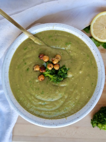 Bowl with blended broccoli soup and parsley too garnish and a spoon inside and roasted chickpeas on top.