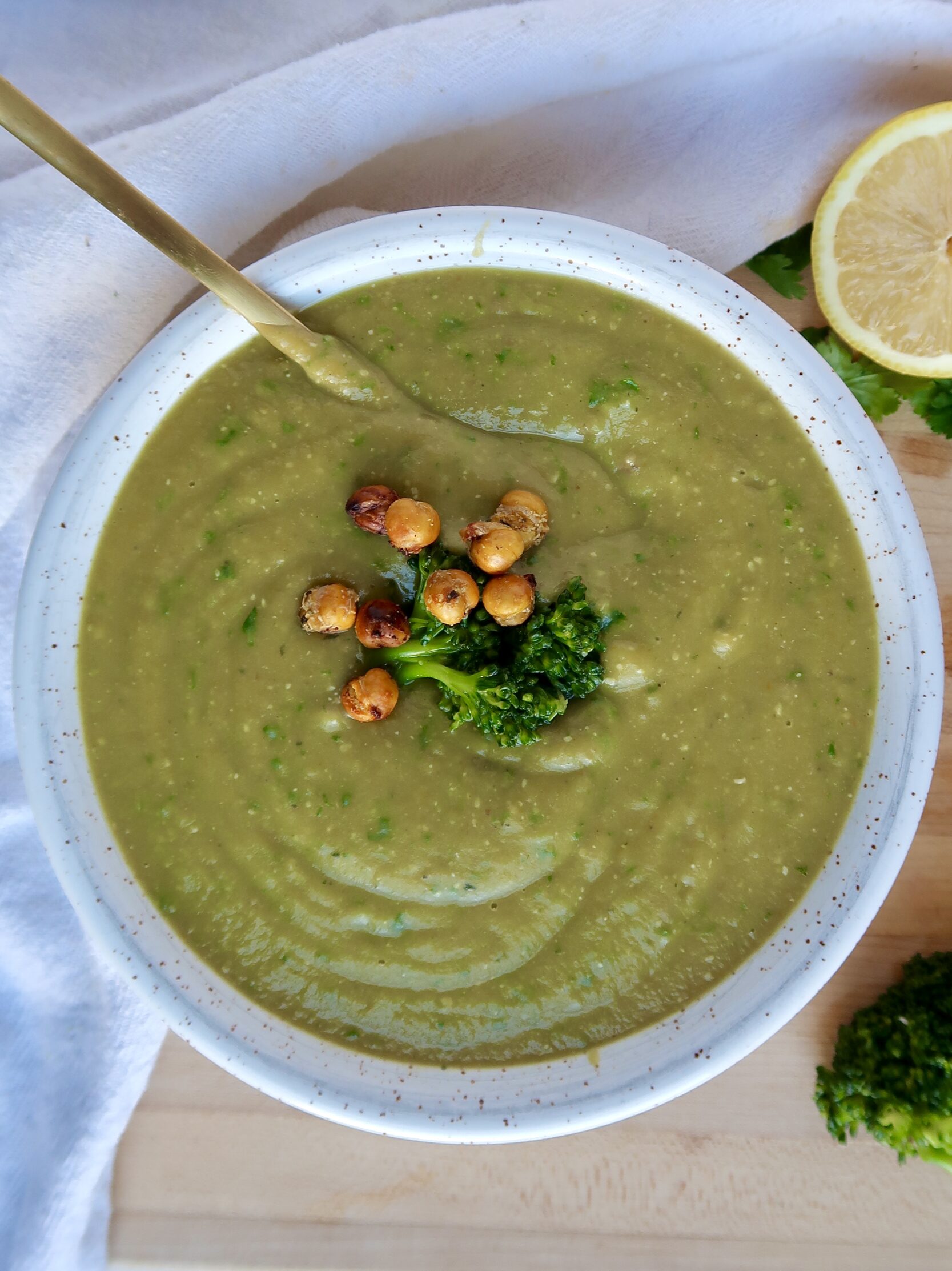 Bowl with blended broccoli soup and parsley too garnish and a spoon inside and roasted chickpeas on top.