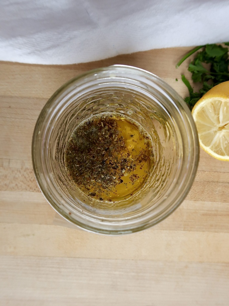 Jar with olive oil and herbs inside with a lemon off to the side.