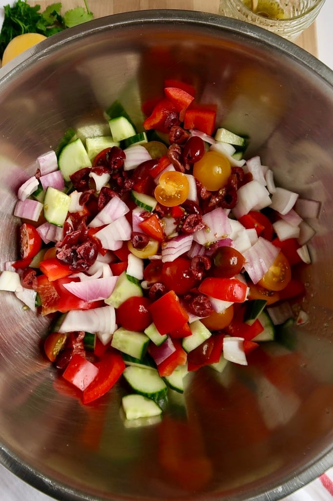 Metal bowl with cucumber, kalamata olives, cherry tomatoes and red onions inside.