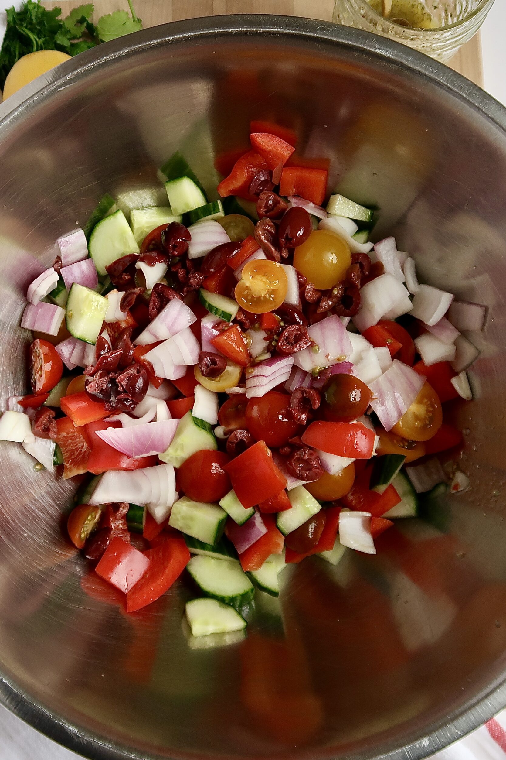Metal bowl with cucumber, kalamata olives, cherry tomatoes and red onions inside.