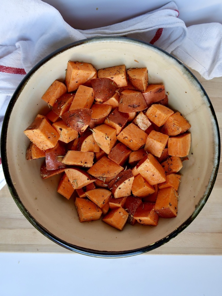 Cubed sweet potato in a large bowl with spices mixed in.