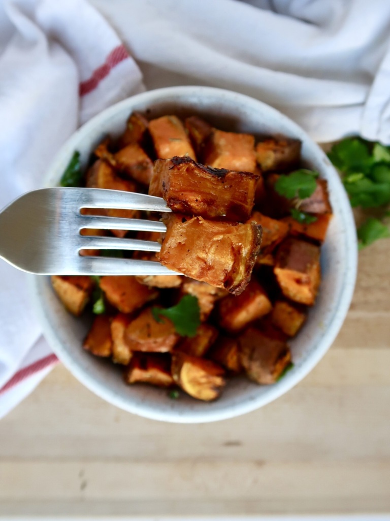 Roasted sweet potato with spices in a bowl with cilantro for garnish and a fork piercing one.
