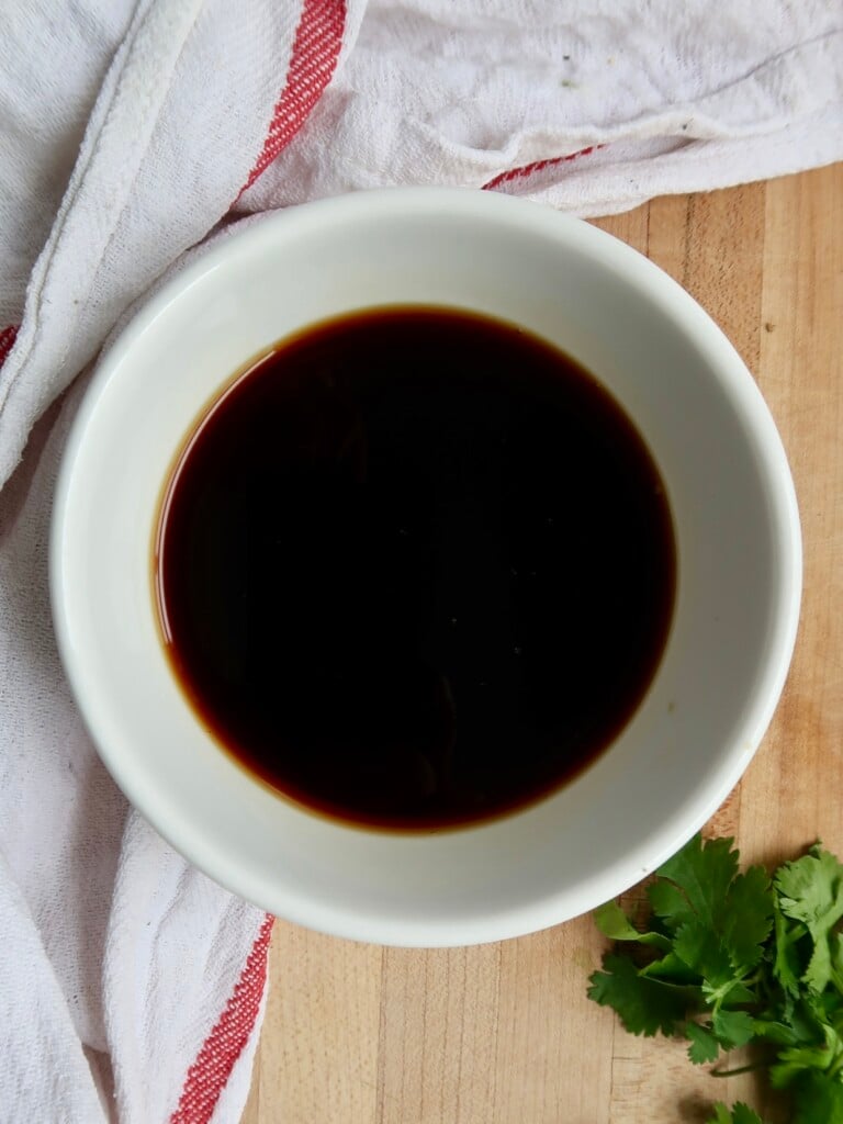 Small white bowl with soy sauce and maple syrup in it.