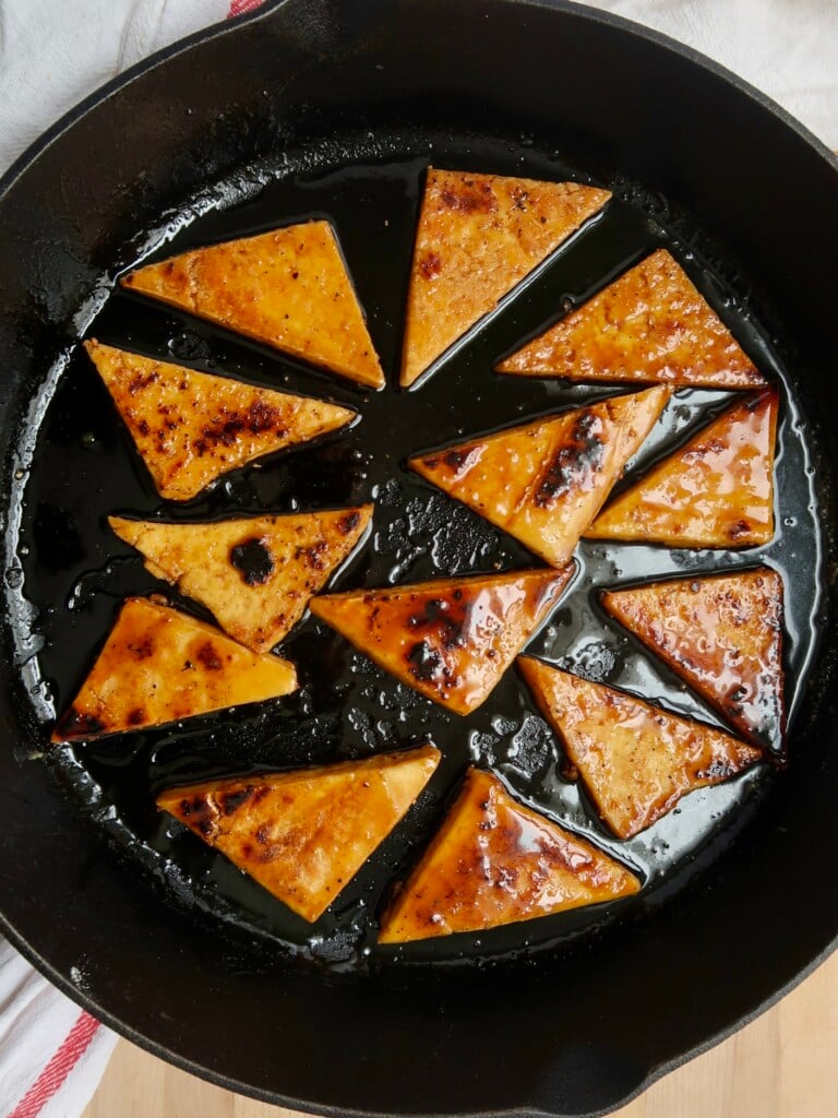Tofu cut into triangles that are in a cast iron pan with a maple glaze on top.