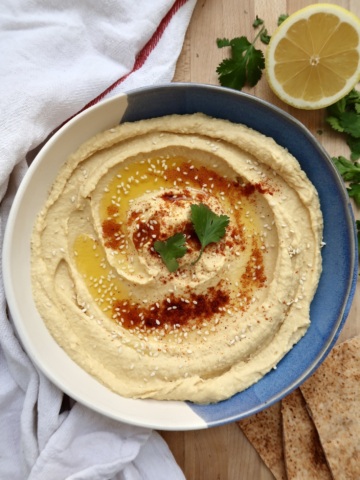 Bowl of hummus garnished with olive oil, paprika, and parsley.