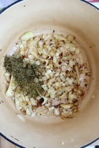 Large pot with diced onion inside and herbs.
