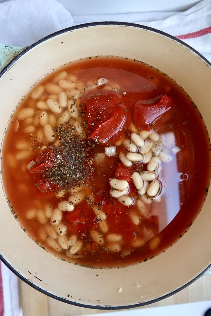 Large pot with broth, white beans, tomato paste and herbs inside.