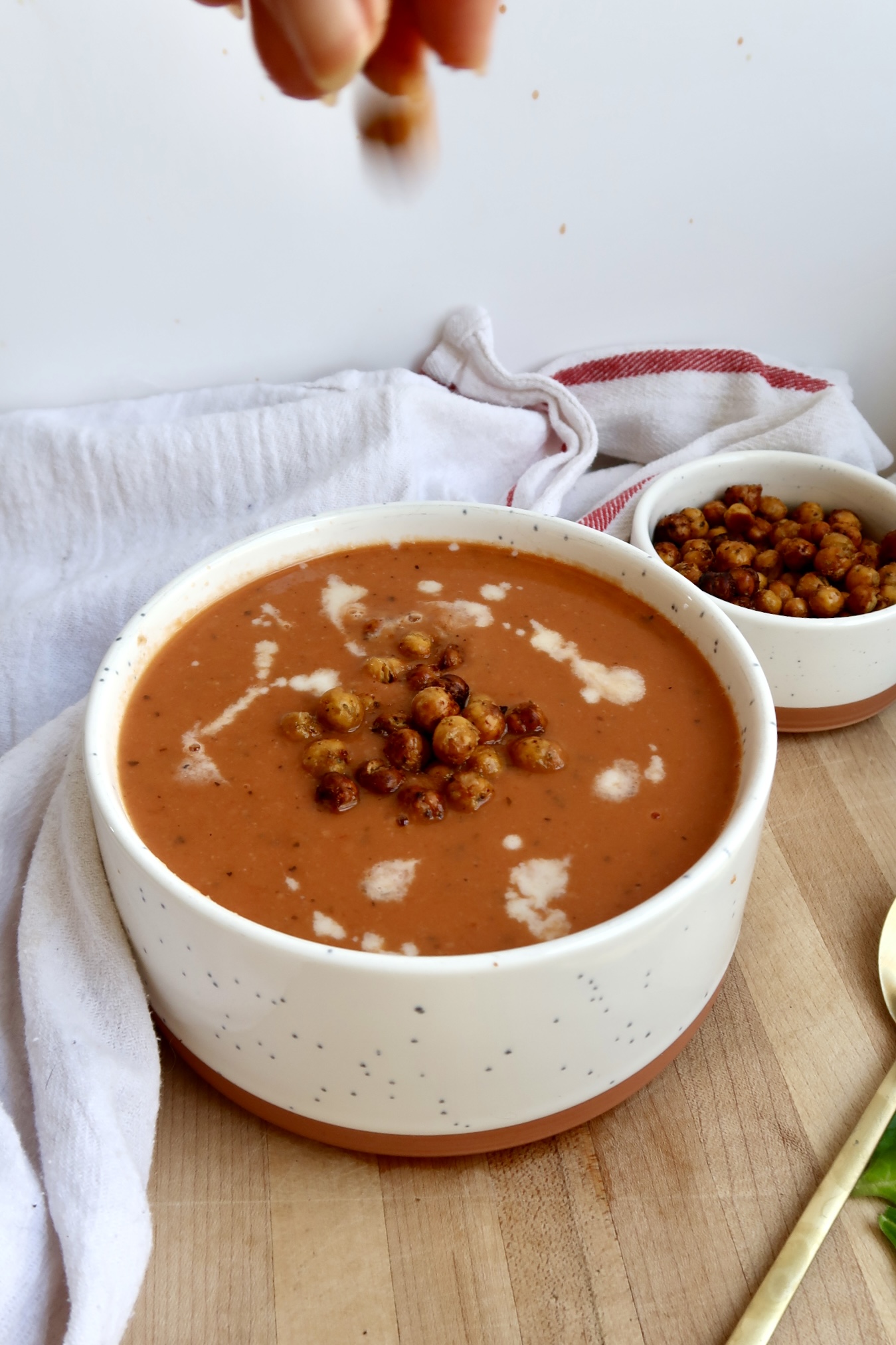 White bowl with tomato soup inside with coconut milk drizzled on top and crispy chickpeas on top with crispy chickpeas in the background.