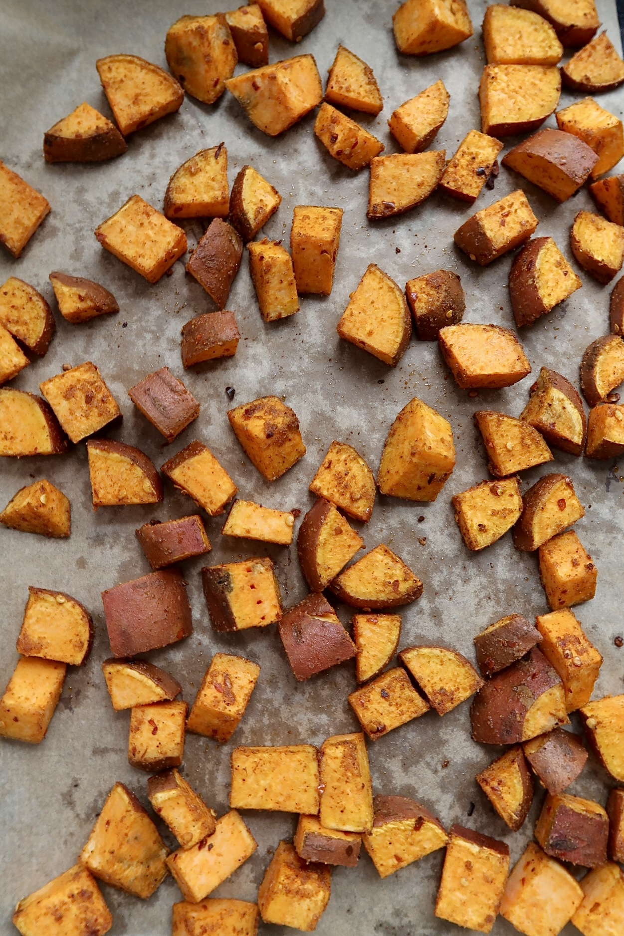 Sheet pan with cooked diced sweet potato with seasonings.
