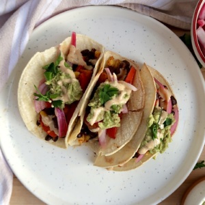 Three tacos with black beans, red onion, avocado, bell pepper and cilantro.
