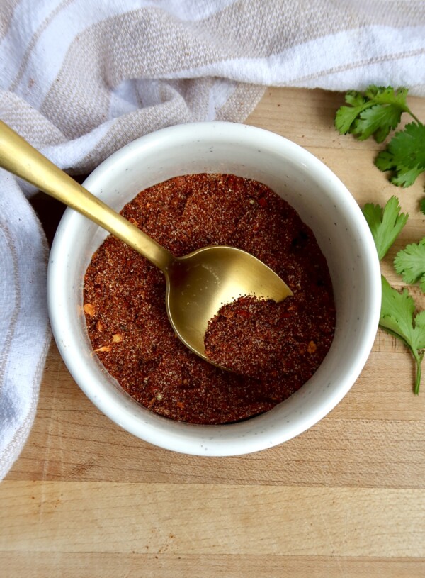 White ramekin with chili spices in it with a spoon in it.
