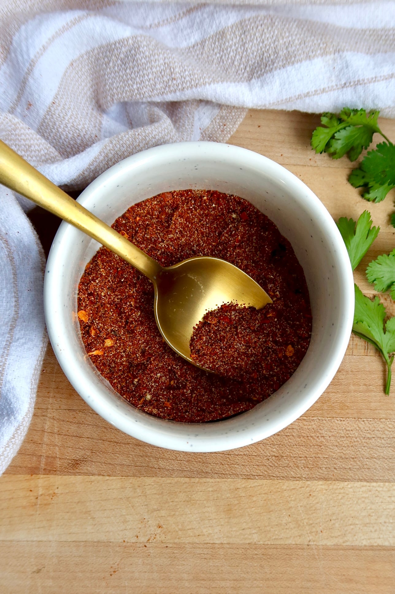 White ramekin with chili spices in it with a spoon in it.