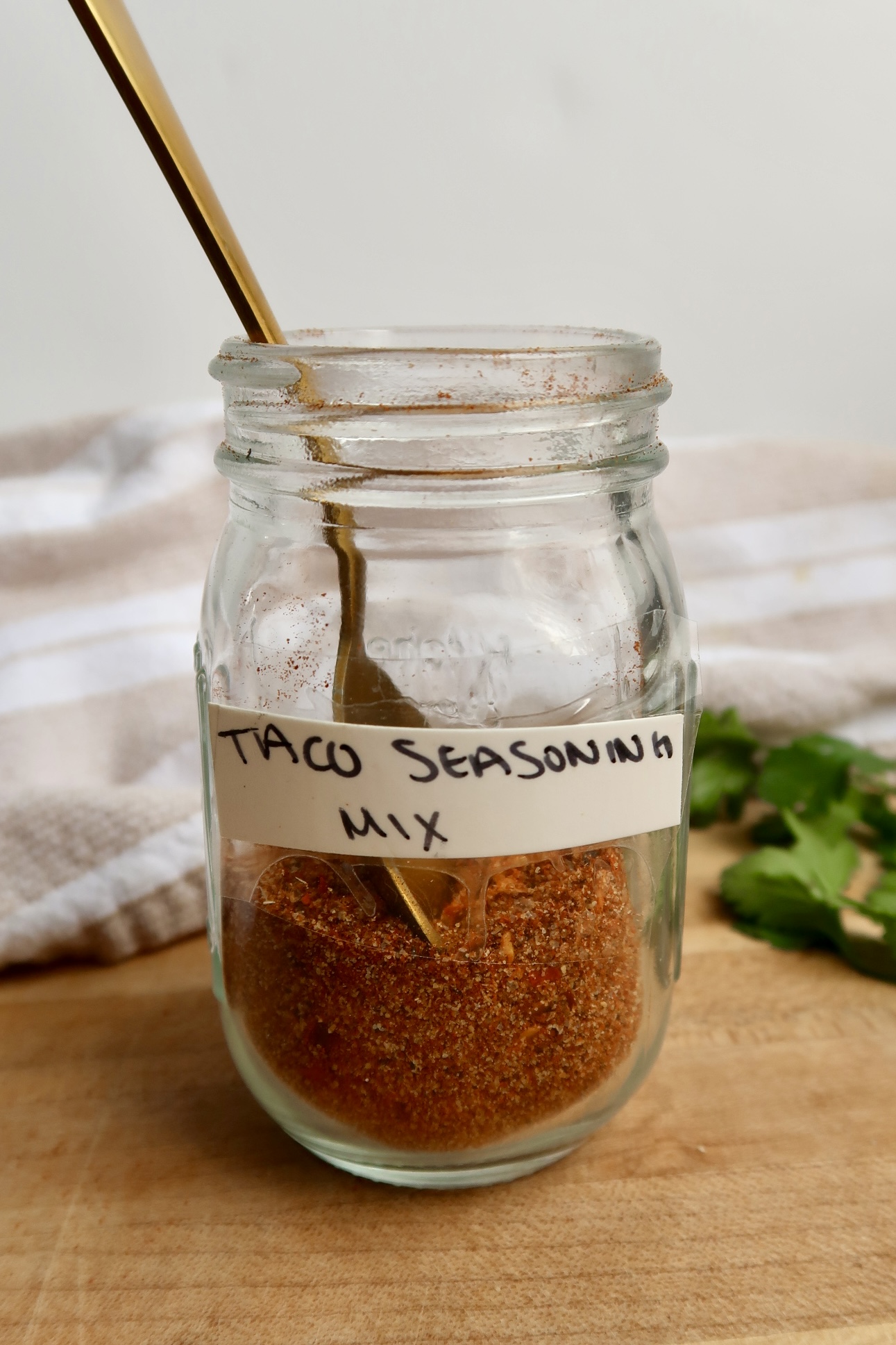 Small clear jar labeled 'taco seasoning mix' with spices in it and a spoon.