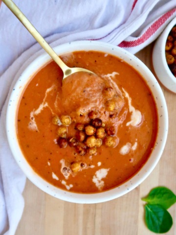 White bowl with tomato soup inside with crispy chickpeas and a spoon in it.