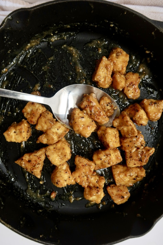 Cast iron pan with saucy tofu in it and a spoon scooping some.