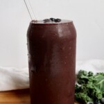 Blueberry kale smoothie in a glass with a straw and blueberries as toppings.