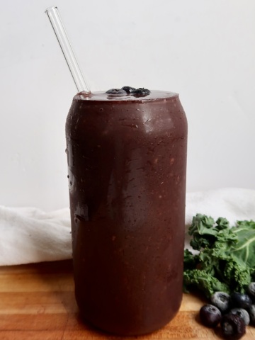 Blueberry kale smoothie in a glass with a straw and blueberries as toppings.