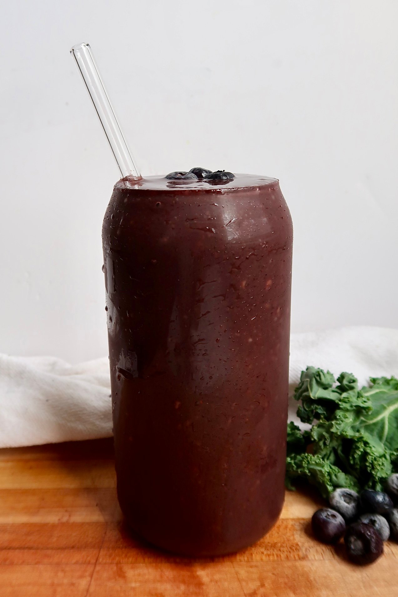 Blueberry kale smoothie in a glass with a straw and blueberries as toppings.