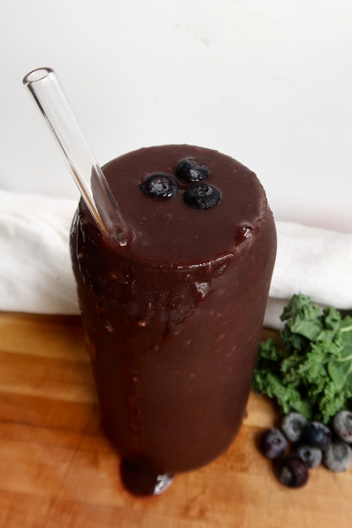Top view of Blueberry kale smoothie in a glass with a straw and blueberries as toppings.