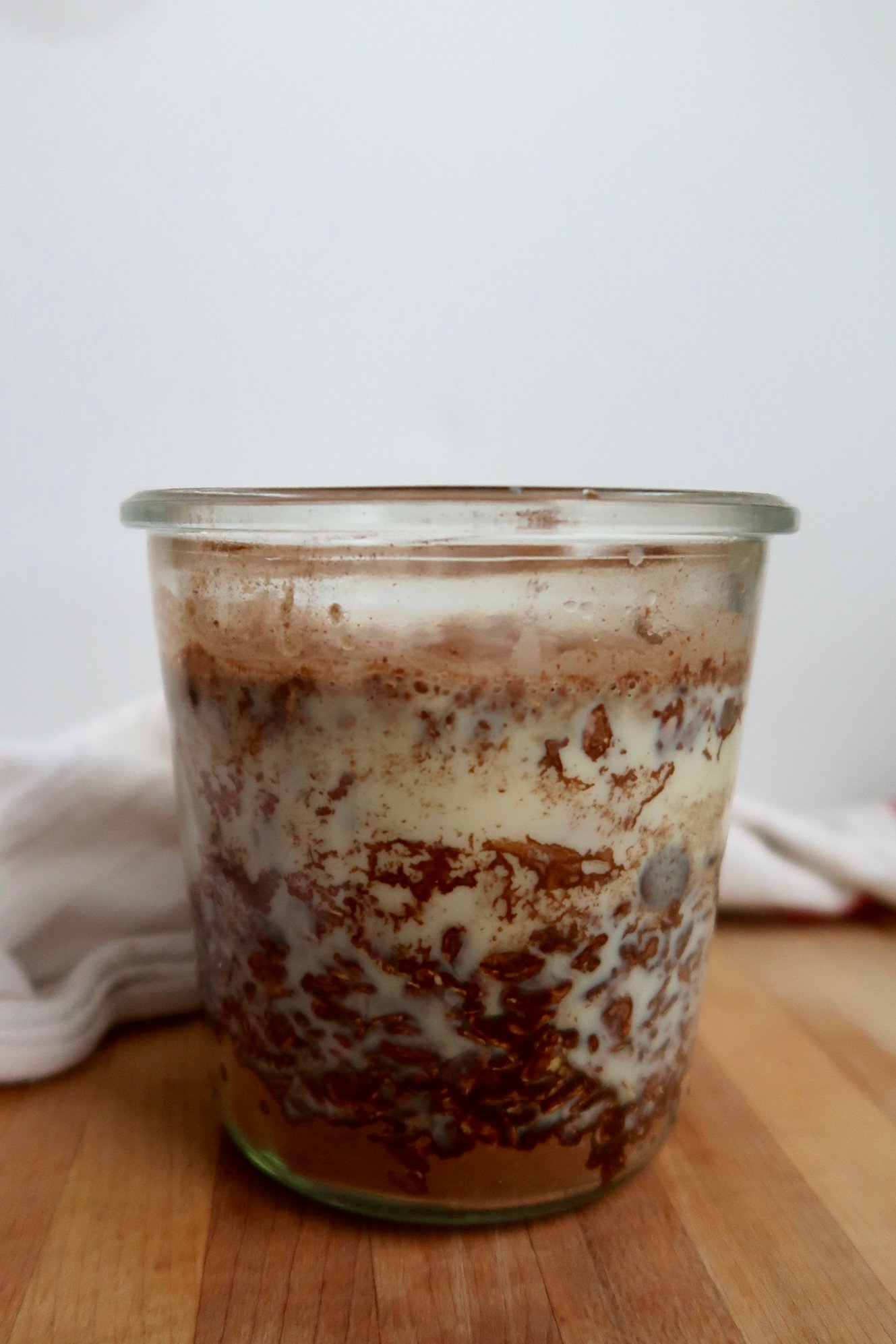 Glass jar with oats, soy milk and cocoa powder in it.