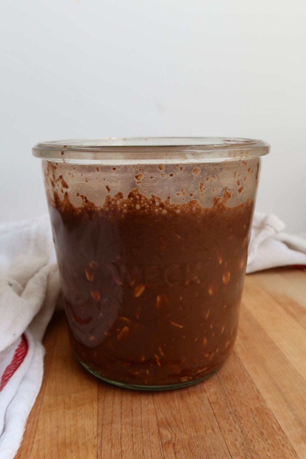 Glass jar with chocolate plant based milk and large flake oats mixed in.
