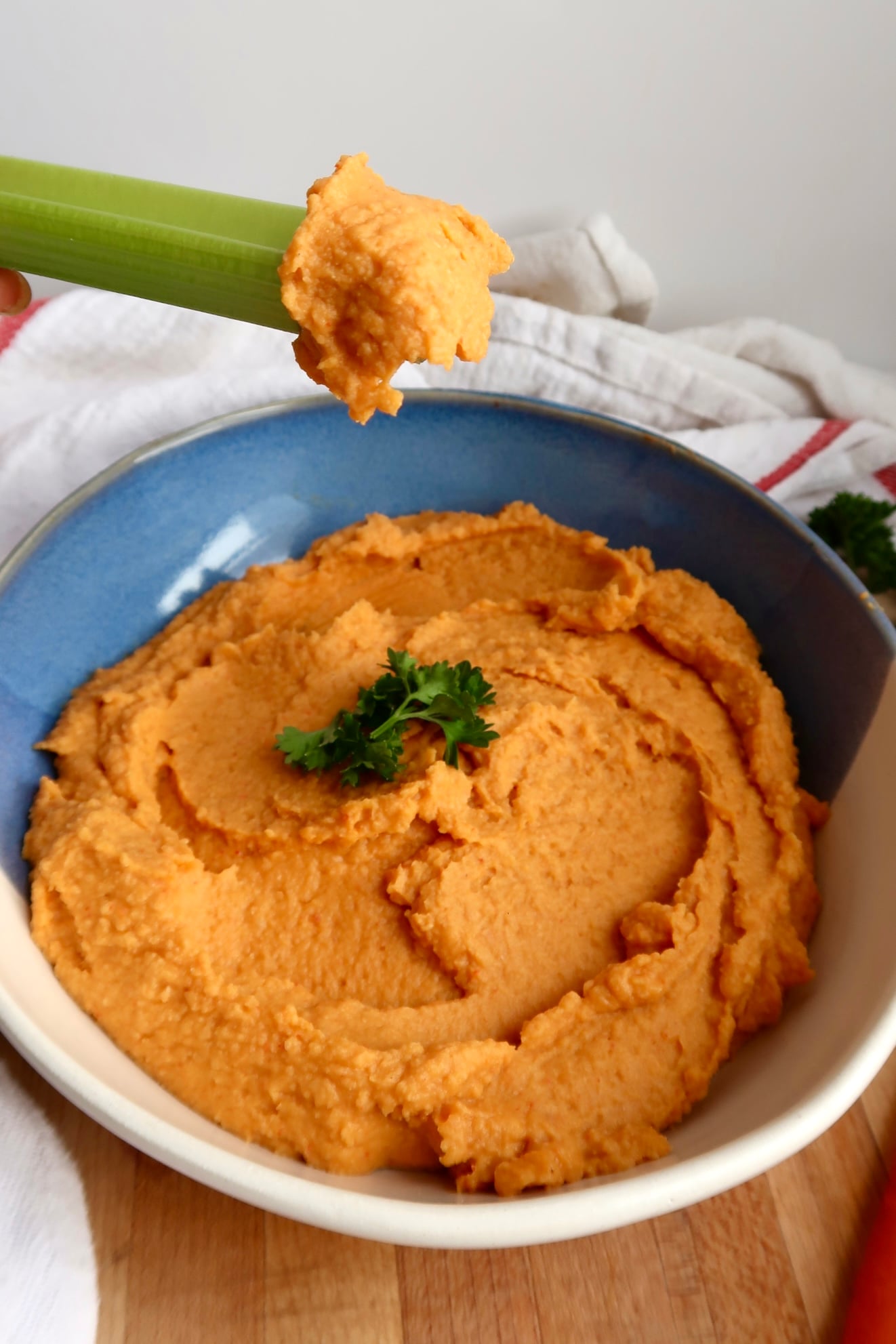Side view of bowl with buffalo chickpea dip and parsley on top with celery dipped.